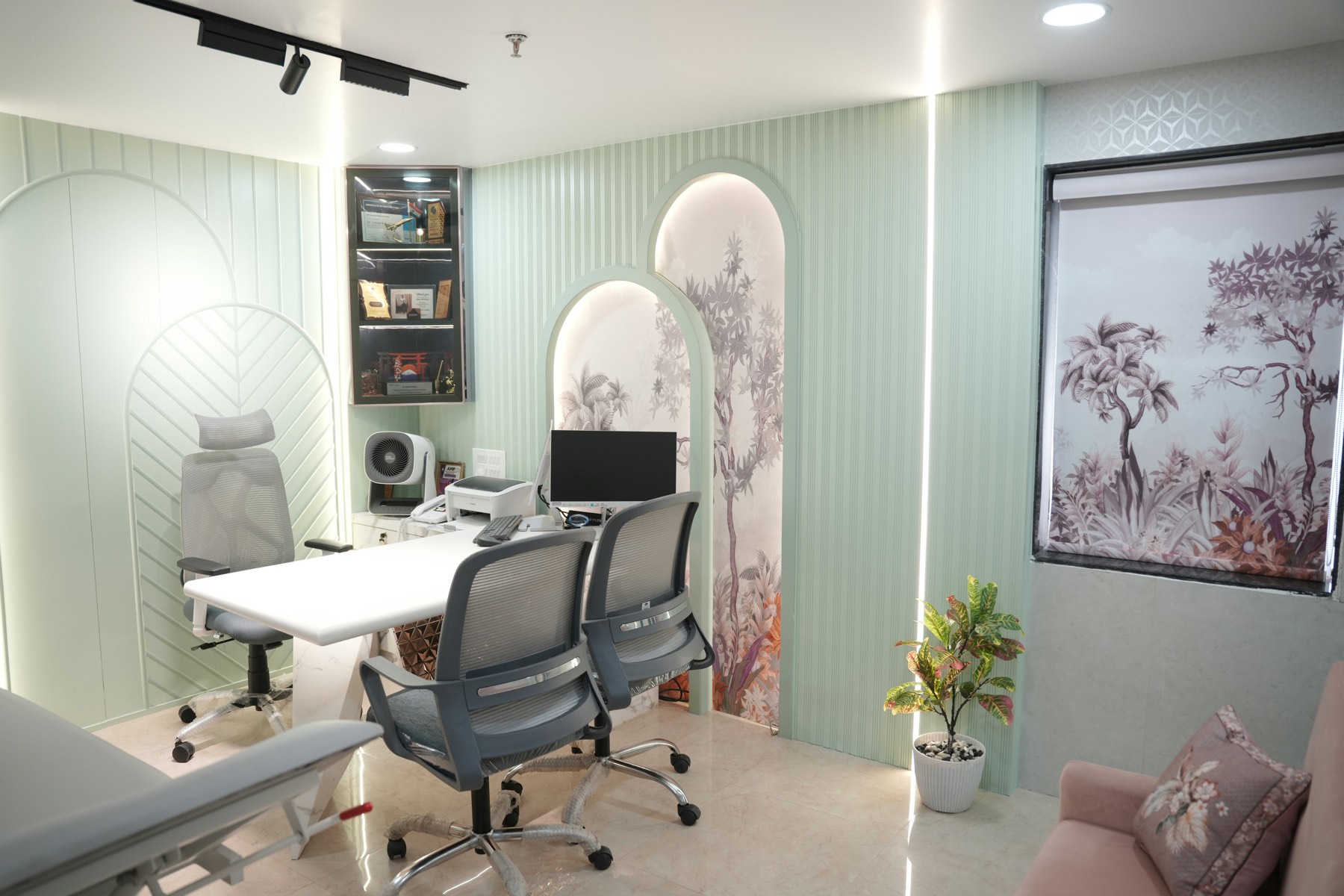 A consultation room with a desk, two chairs and a treatment bed.